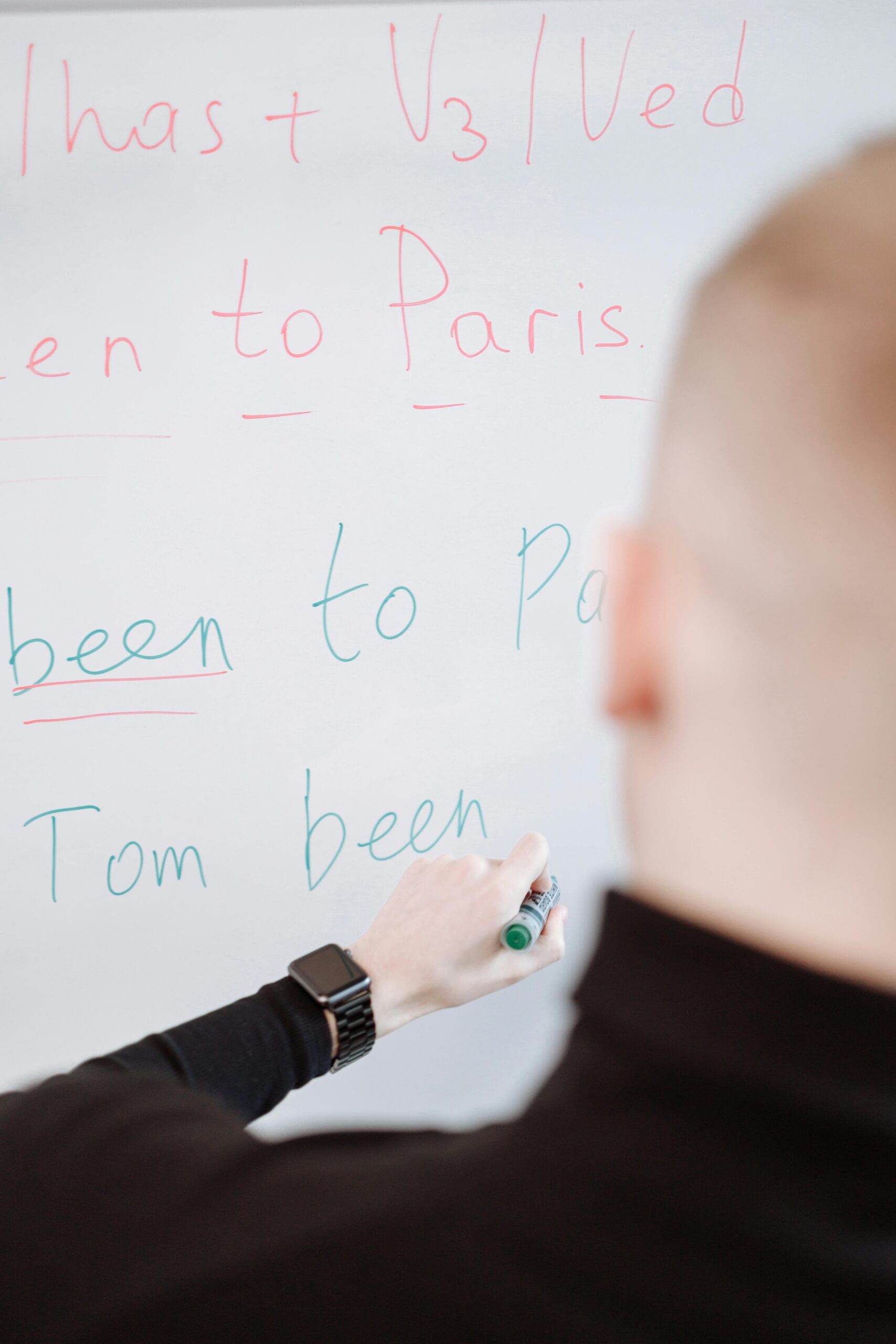 A person writing grammar instructions on a whiteboard with a marker.